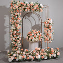 Boules de roses simulées orange et rose avec de longues rangées de fleurs disposées sur le site du mariage, décorées d'arches en fer et de fleurs simulées